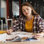 Image of serious caucasian girl doing homework with exercise books