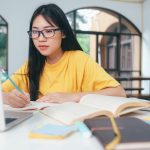 Young collage student using computer and mobile device studying online.